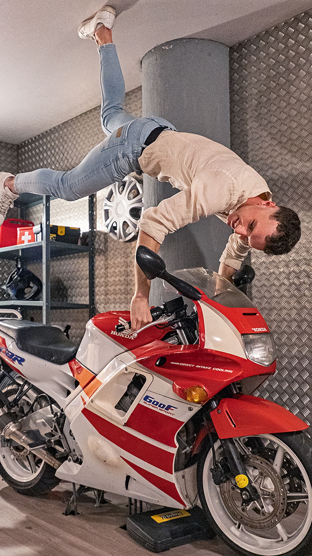 Young man balancing upside down on a red-and-white Honda sports motorbike mounted to the ceiling of a garage at Upside Down House Barcelona